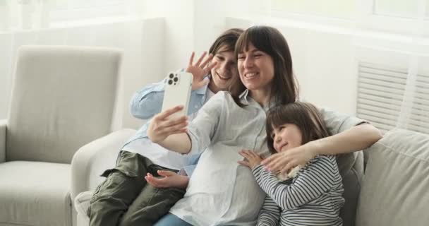 バーチャルビデオ通話のためにソファに集まる白人の家族 妊娠中の母親は 息子や娘と一緒に 画面を通して会話や心からの交流を行っています — ストック動画