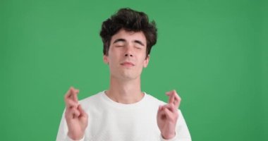 Umut dolu beyaz bir adam canlı yeşil bir zemine karşı. Kendinden emin bir gülümseme ile parmaklarını birbirine geçirir ve onları çapraz yapar. Bu umut ve olumlu beklentinin bir göstergesidir..