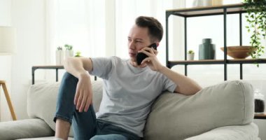 Neşeli bir beyaz adam bir kanepede oturuyor ve bir telefon görüşmesi yapıyor. Yüzünde parlak bir gülümsemeyle, iletişim kurarken mutluluk ve coşkuyu ifade eder..