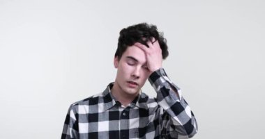 Beyaz arka planda kıvırcık saçlı, beyaz saçlı bir adam. Yüzünde hüsran ve istifanın bir karışımıyla ayakta duruyor. Hızlı bir hareketle, avucunu yüzüne doğru klasik bir facepalm hareketi yapıyor..