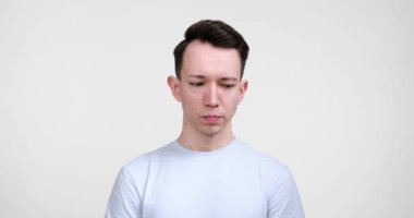 Beyaz bir arka plana karşı duran ciddi bir beyaz adam, düşüncelerinde kaybolmuş. Dalgın kaşlar ve kasvetli bir ifade onun iç gözlem derinliğini ortaya koyuyor..