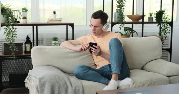 Hombre Está Sentado Cómodo Sofá Sala Estar Lleva Par Audífonos — Vídeos de Stock