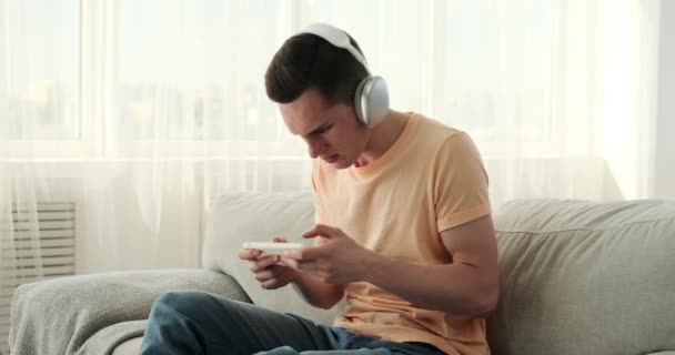 Młody Biały Mężczyzna Głęboko Pochłonięty Ekscytującą Mobilną Grą Leżąc Kanapie — Wideo stockowe