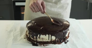 Adam ustalıkla çikolatalı kremayı pastanın üstüne serpiyor. Sabit bir el ve sanatsal bir dokunuşla, kaşık kullanarak kadife çikolatalı kremayı pastanın üzerine döker..