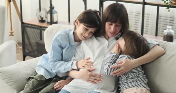 妊娠中の母親は息子と娘と一緒にソファに座っている 笑顔で つながりと愛の瞬間を共有します 一緒に 彼らは優しく 母親が腹を成長愛撫 — ストック動画