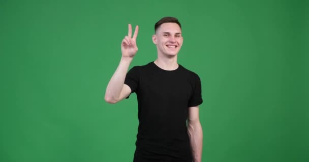 Zielonym Tle Młody Biały Mężczyzna Dumą Pokazuje Znak Zwycięstwa Uśmiechem — Wideo stockowe