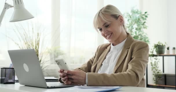 人们看到快乐的白人女商人在办公室里带着灿烂的笑容用她的手机 她生气勃勃的情绪和快乐的举止反映了沟通或成功对话的乐趣 — 图库视频影像