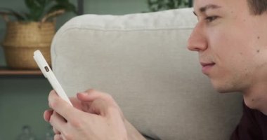 Oturma odasındaki kanepede oturan bir adam, kahkahalara boğulurken telefonuyla canlı mesajlaşırken görülüyor. İçten gülüşü sohbette bulduğu zevki gözler önüne seriyor..