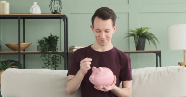 Seorang Pria Yang Bahagia Ditunjukkan Meletakkan Koin Dalam Celengan Babi — Stok Video