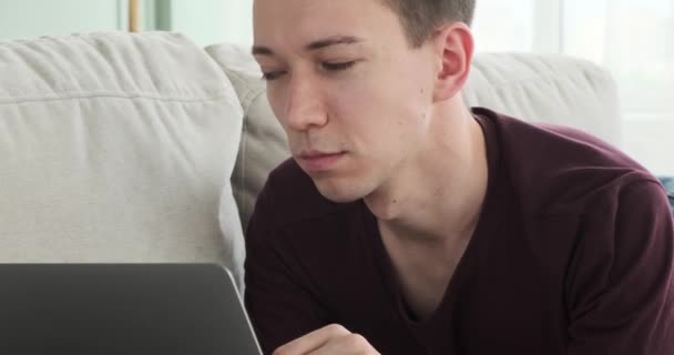 Genç Beyaz Bir Adam Kanepeye Uzanmış Bilgisayarında Neşeli Bir Gülümsemeyle — Stok video
