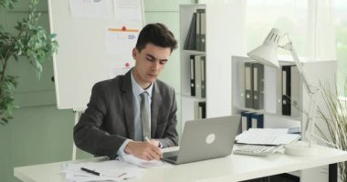 Stern Kafkasyalı işadamı çalışma masasında oturmuş, özenle kağıtları yazarken görülüyor. Odaklanmış ve ciddi bir ifadeyle, belgeleri titizlikle hallediyor..