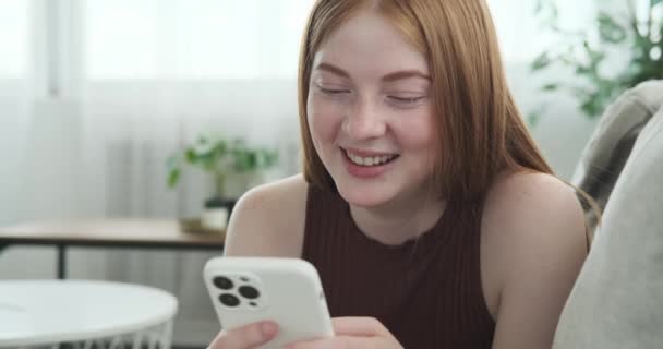 Egy Vörös Hajú Lány Szívből Nevet Miközben Kanapén Fekszik Telefonnal — Stock videók