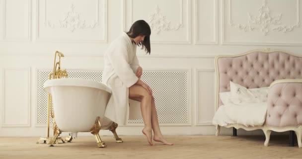 在浴室里 一个白人女人沉溺于一场爱抚人的活动中 在她的手上和腿上轻轻按摩奶油 浴室舒适的氛围提供了一种放松和舒适的感觉 — 图库视频影像