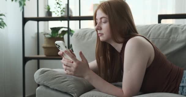 Vörös Hajú Tinédzser Lány Láthatóan Unatkozik Miközben Kanapén Fekszik Telefonjával — Stock videók