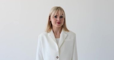 Beyaz bir arka planda beyaz bir kadın, gülümseyerek parmaklarını dudaklarına dayayarak şşş hareketi yapıyor. Onun sıcak ifadesi ve dostane tavırları gizlilik hissi yayıyor..