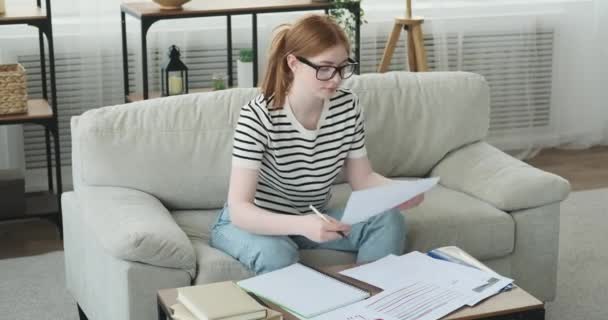 Ένα Συγκεντρωμένο Έφηβο Κορίτσι Φαίνεται Δουλεύει Επιμελώς Χαρτιά Στο Σαλόνι — Αρχείο Βίντεο