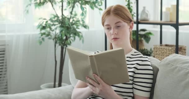 Muchacha Adolescente Sonriente Representa Sentado Sofá Totalmente Absorto Lectura Libro — Vídeo de stock