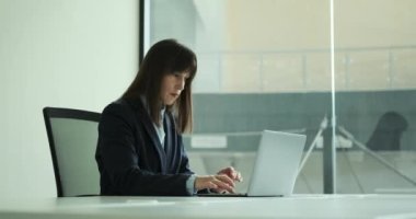 Kurumsal bir ortamda, kafası karışmış bir iş kadını zorlu bir görevle karşı karşıya olduğu için dizüstü bilgisayara dalmış bir şekilde masada oturuyor. Düşünceli ifadesi bir çözüm bulma kararlılığını yansıtıyor..