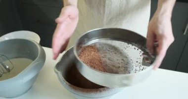 Adam mutfak masasındaki süzgeçten kakao tozunu süzüyor. Odaklanmış bir bakışla ve nazik el hareketleriyle kakaonun ince ayıklanarak yumuşak ve kadife bir dokuya dönüşmesini sağlar..