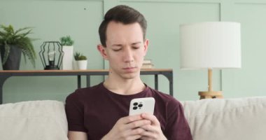 Düşünceli genç bir adam kanepede otururken telefonla yakalanır. Yüzü yoğunlaşmayı ve düşünmeyi yansıtıyor. Bakışları telefon ekranına sabitlenmiş..