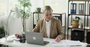 Yetenekli bir iş kadını, defterine önemli notlar yazarken dokümanları verimli bir şekilde yönetirken görülüyor. Odaklanmış bir tavırla, evrak işlerini uzmanlıkla hallediyor..