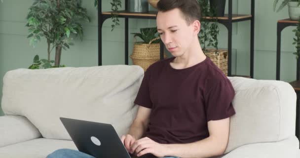 Homem Está Sentado Sofá Digitando Seu Laptop Enquanto Olha Para — Vídeo de Stock