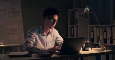 Odaklanmış yönetici özenle dizüstü bilgisayarında yazarken görülüyor. Ekranın yumuşak parıltısı, önemli görevler için çalışırken onun dikkatli yüz ifadesini aydınlatır..