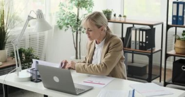 İş kadını ofisinde meşgul, aciliyet duygusuyla belgelere hızlıca göz gezdiriyor. Görevlerde hızlı hareket ederken, odaklanması ve kararlılığı bariz..