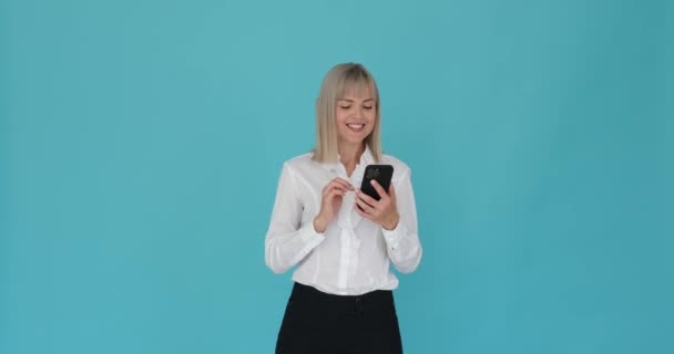 Femme Optimiste Est Naviguant Joyeusement Son Téléphone Sur Fond Bleu — Video