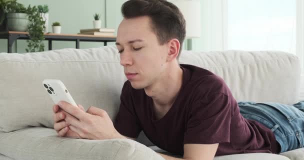 활기차고 즐거운 장면에서 행복한 코카서스 사람은 소파에 누워있는 전화에서 메시징을 — 비디오