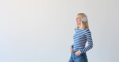 Beyaz kadın temiz beyaz bir arka planda, kulaklık takıyor ve müzikten hoşlanıyor. Rahatlamış ifadesi ve ince kafa hareketleri müziğe olan bağlılığını gösteriyor..