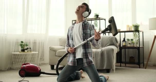 人在打扫房子的时候变成了摇滚明星 他带着一把扫帚或吸尘器作为他的空气吉他 展现了一个真正的摇滚传奇的魅力和舞台风采 — 图库视频影像