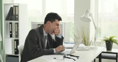 Yorgun Kafkasyalı ofis çalışanı masasında otururken esnerken yakalandı. Yüzündeki ifade yorgunluğu yansıtıyor ve esnemesi dinlenme ve gençleşme ihtiyacını gösteriyor..