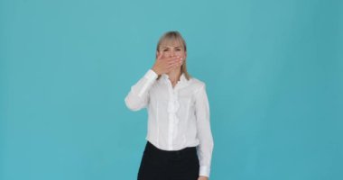 Kendine güvenen bir kadın, eli ağzını kapatıyor, kendini susturuyor, sakinleştirici mavi bir arka plana karşı. Kendine güveni tam ifadesi kasıtlı bir gizlilik ya da kısıtlama eylemine işaret ediyor..