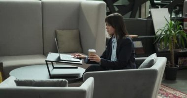 Canlı bir çalışma alanında, Kafkasyalı bir iş kadını dizüstü bilgisayarıyla oturur, tamamen işine dalmıştır. Yanında bir fincan kahve oturarak rahatlatıcı bir enerji kaynağı sağlıyor..
