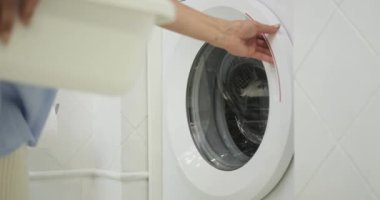 Becerikli bir kadın ev işlerinin sorumluluğunu üstlenir ve kirli giysileri çamaşır makinesine yükler. Odaklanmış tavrı, düzenli bir ev ortamındaki kararlılığını yansıtıyor..