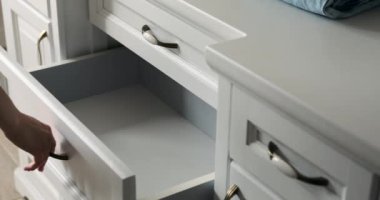 Nazik bir dokunuşla, bir kadın özel eşyalarını şifonyer çekmecesine titizlikle yerleştirir. Özenli tavrı, içeriği özenle düzenlediği için ortalığı toparlama sanatının bir örneği..