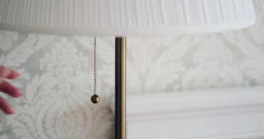 Zarif bir dokunuşla, bir kadın elleri zarif bir şekilde bir lambayı çalıştırır, odanın içinde yumuşak ve davetkar bir parıltı yayar. Onun jesti işlevselliği estetikle harmanlıyor, ambiyansı güçlendiriyor..