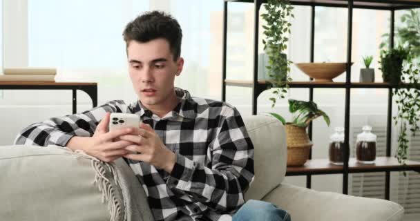 Siedząc Kanapie Niezadowolony Mężczyzna Podejmuje Rozmowę Sms Ową Przez Telefon — Wideo stockowe