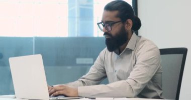 Ciddi bir havayla, bir işadamı kendisini ofis içinde dizüstü bilgisayarda yazmaya adadı. Odaklanmış bakış ve hassas tuş vuruşları onun fikirleri dijital forma çevirmedeki kararlılığını yansıtıyor..