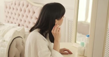 Beyaz bir kadın pamuk çubuğu kullanarak dikkatle kulaklarını temizliyor. Odaklanmış ve dikkatli bir yaklaşımla, nazik hijyen ve temizlik sağlar. Kamera onun hareketlerinin hassasiyetini yakalar..