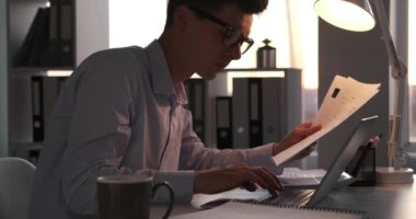 Meşgul işadamı bir yığın kağıtla özenle çalışırken görülüyor. Davranışları ve düzenli çalışma alanı, elindeki görevlere olan bağlılığını yansıtıyor..