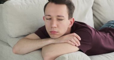 Dokunaklı bir görüntüyle, üzgün bir beyaz adam kanepede yatarken tasvir edilir. Yüzü hüzün ve melankoliyi yansıtıyor, gözleri duygularının derinliğini yansıtıyor..