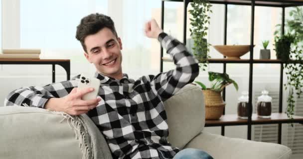 Kanepede Oturan Beyaz Bir Adam Telefonunu Tutarak Bir Başarıyı Sevinçle — Stok video
