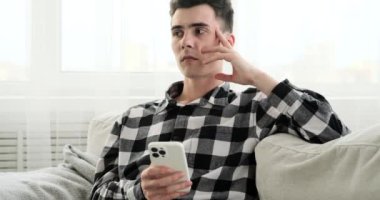 Kanepede dinlenen, üzgün bir genç adam telefona sarılırken içsel üzüntüden söz eder. Cihaz hem teselli kaynağı hem de duygusal durumu hatırlatan dokunaklı bir sahne yaratıyor..