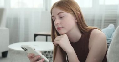 Bir kız, koltukta yatarken telefonuyla mesajlaşırken derin düşüncelere dalmış şekilde tasvir edilir. Onun ifadesi, dijital sohbete girerken içgözlem ve yansıma hissini yansıtır..