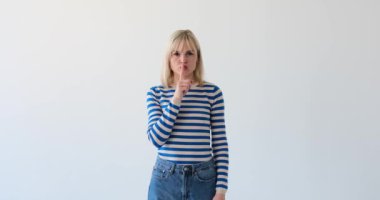 Sert ve ciddi bir kadın temiz beyaz bir arka planda, parmaklarıyla dudaklarına şşşş hareketi yaparken görülüyor. Sert ifadesi ve 