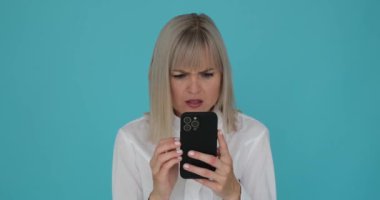 Şaşkın bir kadın telefonunu mavi bir arka planda kullanırken görülüyor. Kızaran yanakları ve belirsiz ifadesi cihazı kullanırken utandığını ya da kafasının karıştığını gösteriyor..