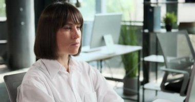 Yakın plan bir portre, ofisteki bilgisayardaki işine odaklanmış kendine güvenen beyaz bir kadını yakalar. Dengeli ve kararlı ifadesi rolündeki yeterliliğini ve profesyonelliğini yansıtıyor..
