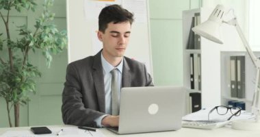 Ciddi girişimciler ofiste dizüstü bilgisayarında özenle yazarken resmediliyor. Onun odaklanmış ifadesi ve kendini işine adamış duruşu işinin önemini yansıtıyor..